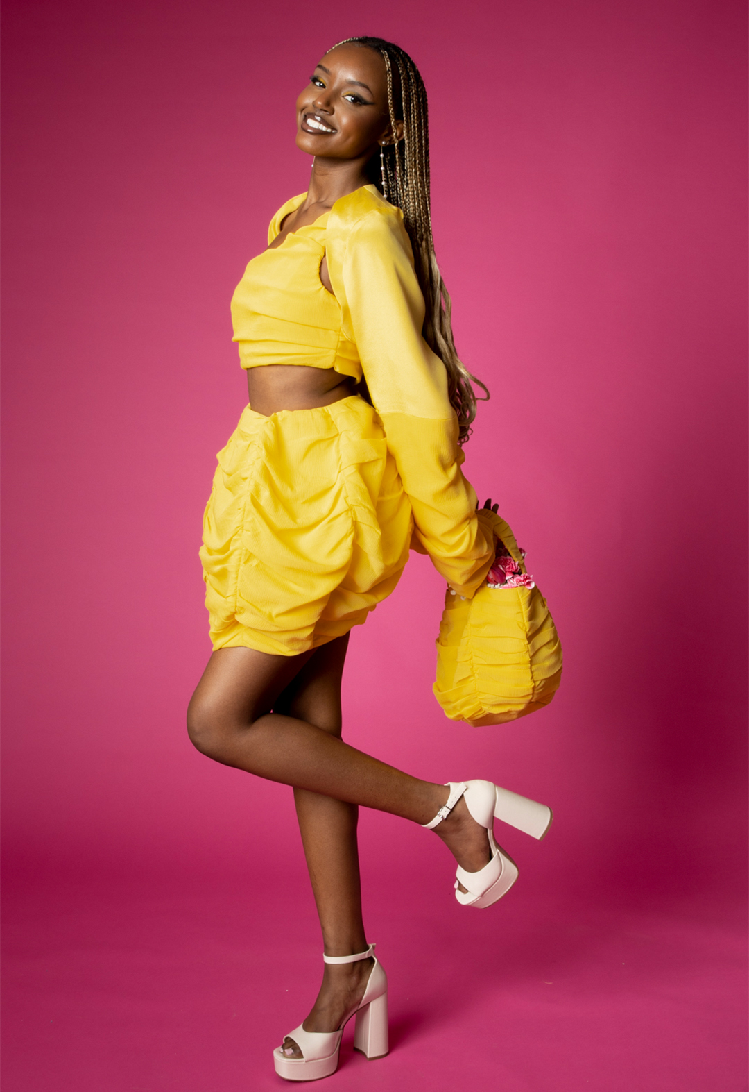 This is a side-view image of a model wearing a yellow silk and crinkle chiffon shrug, a matching one-shoulder ruched top, and a ball skirt.