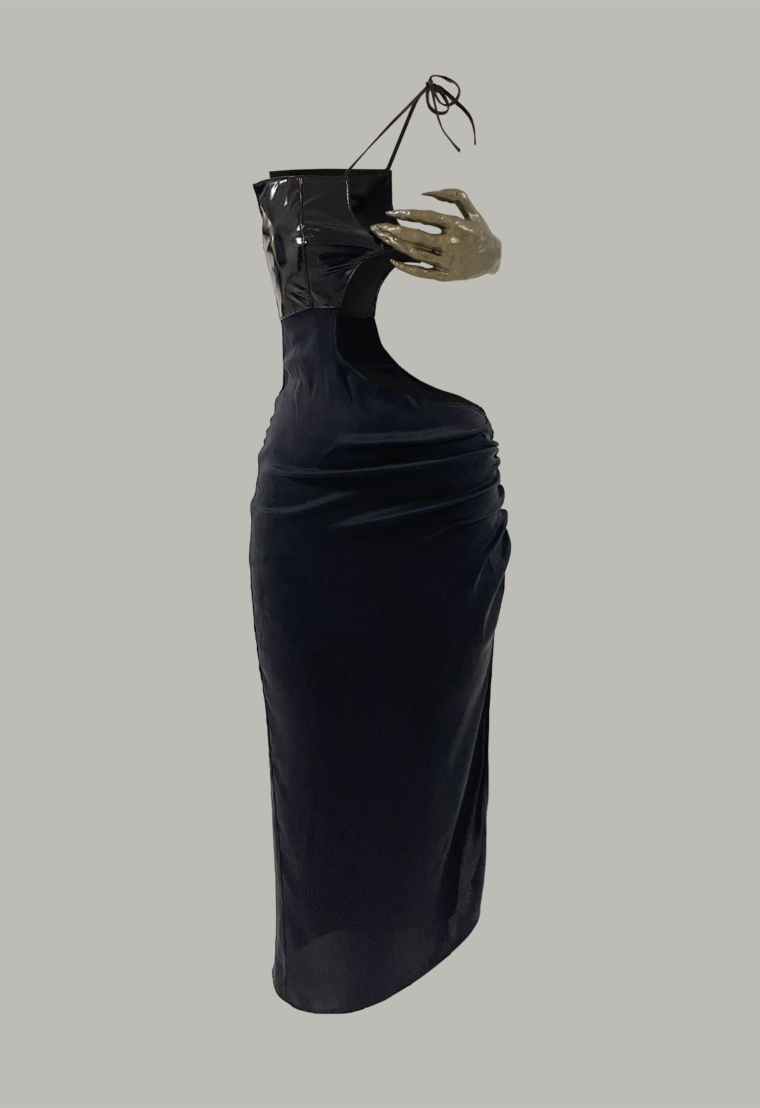 Black asymmetric dress against a light-gray background. The dress has a cutout on the right side of the waist. One strap comes from the bodice and ties diagonally over the shoulder. The bodice of the dress is shiny while the skirt is matte. There is a metallic gold sculpted hand attached to the bodice on the right side at the bust. 