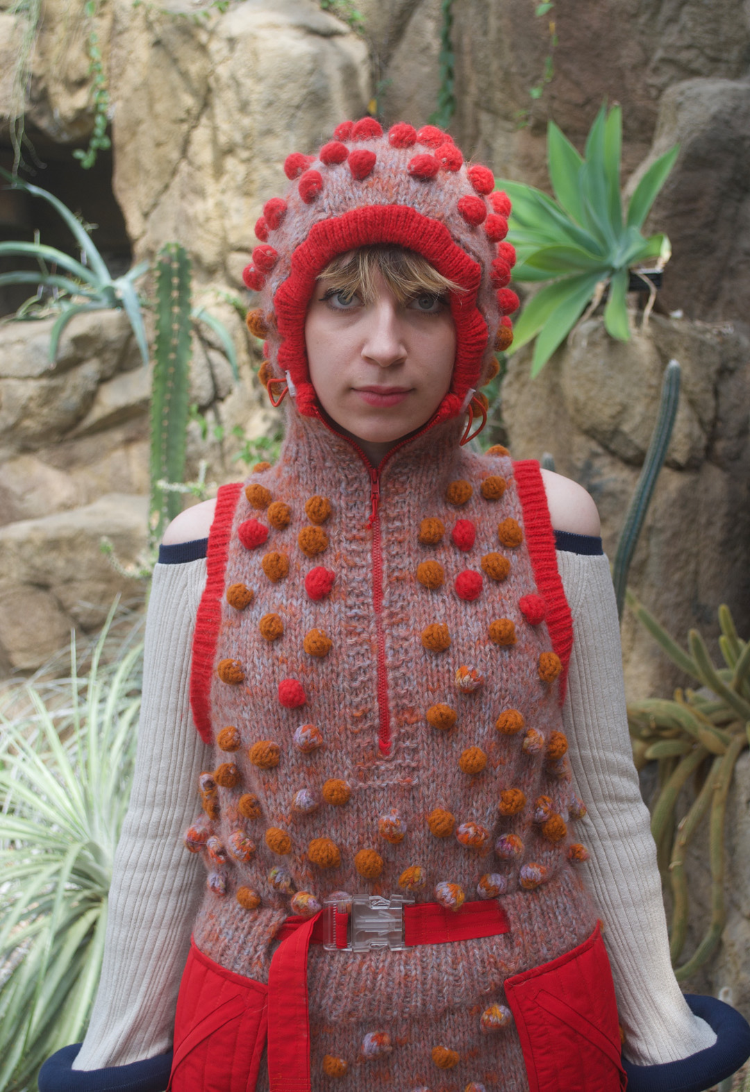 Cropped image of a woman wearing a hand-knit dress with bobbles, hood, and an off-the-shoulder knit top.