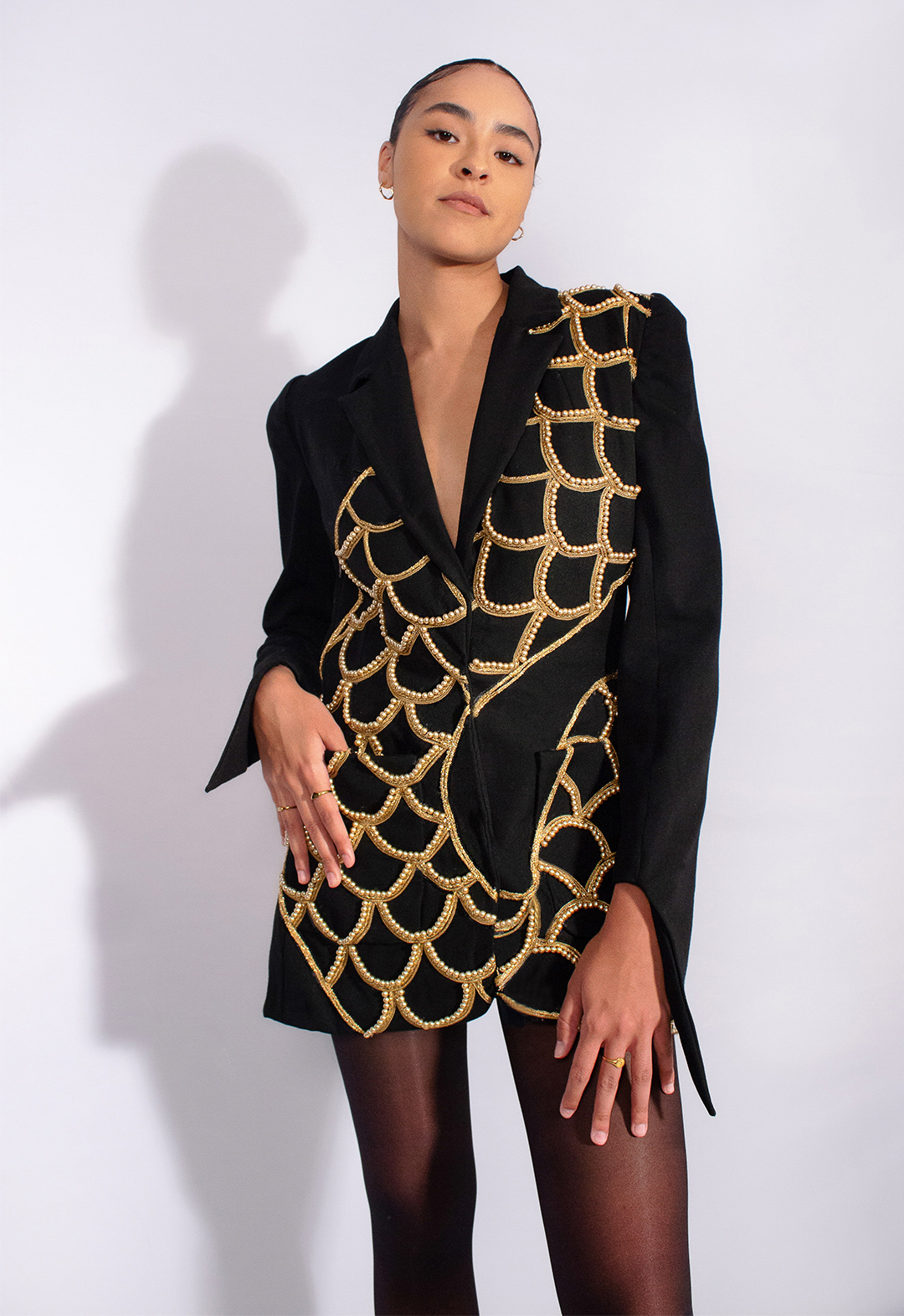 The front view of a black wool jacket portraying the body of the Naga is connected to the back of the jacket. The body is covered in scales that are made out of gold metallic trims and gold glass pearls. It also has a pointed hem on the sleeves.