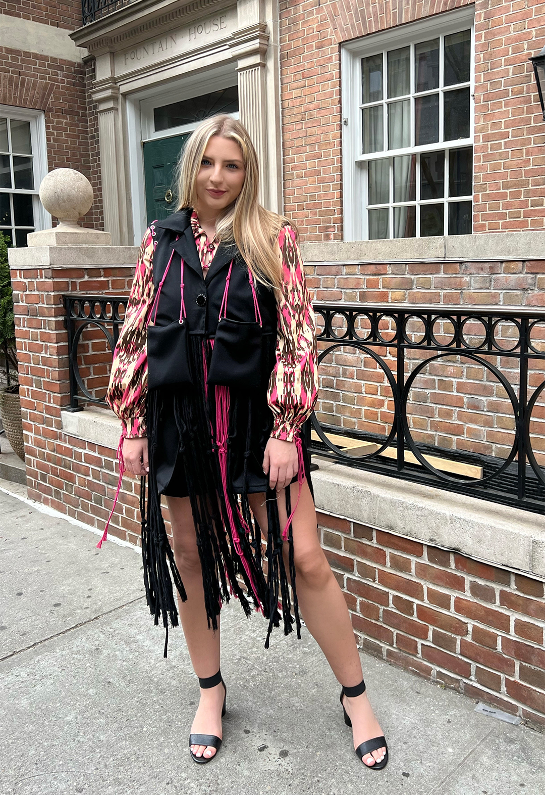 A model wears a button-up top, wide-legged shorts, and a vest blazer with long macramé roping details.