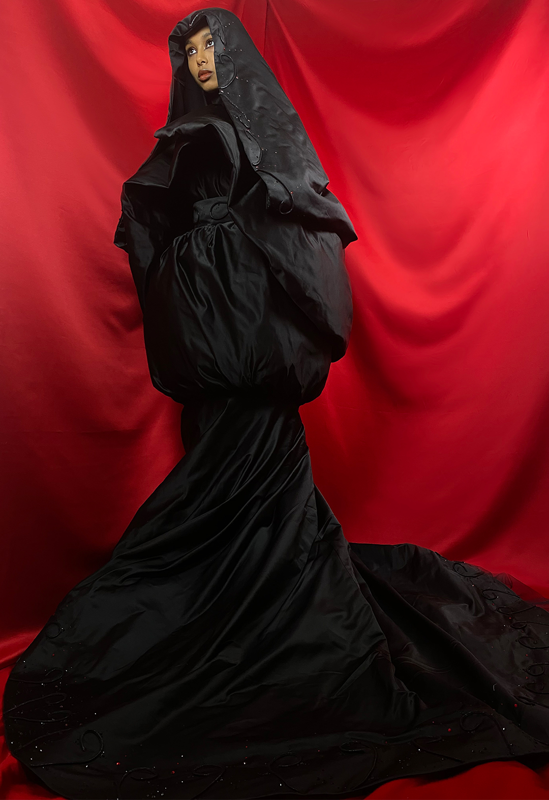 The image shows a front view of a hooded silhouette with the shimmering of hand-applied embellishments on display.