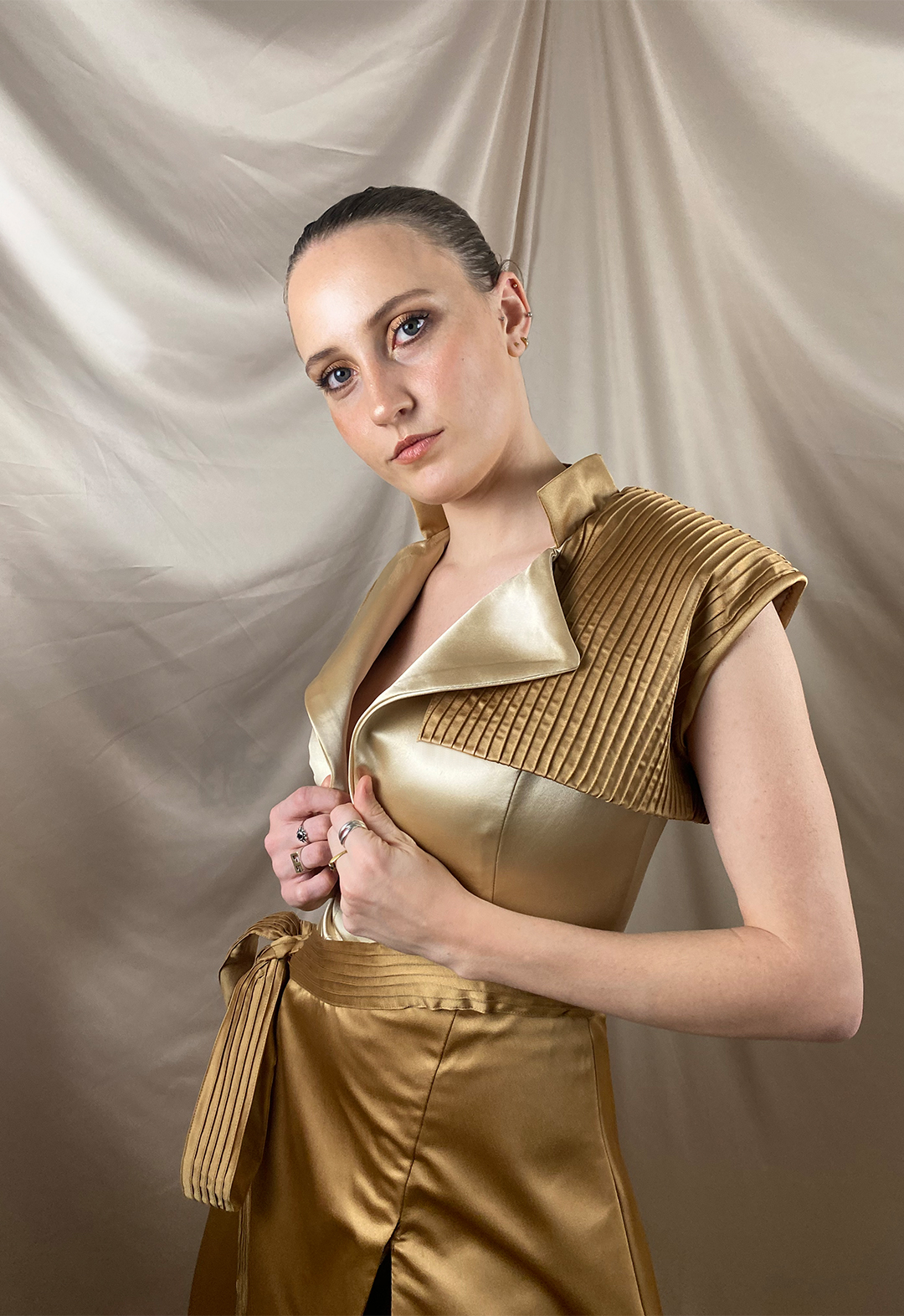 Close-up of a model wearing a two-toned gown with a notched collar bodice, with a pin-tucked vest and belt. 