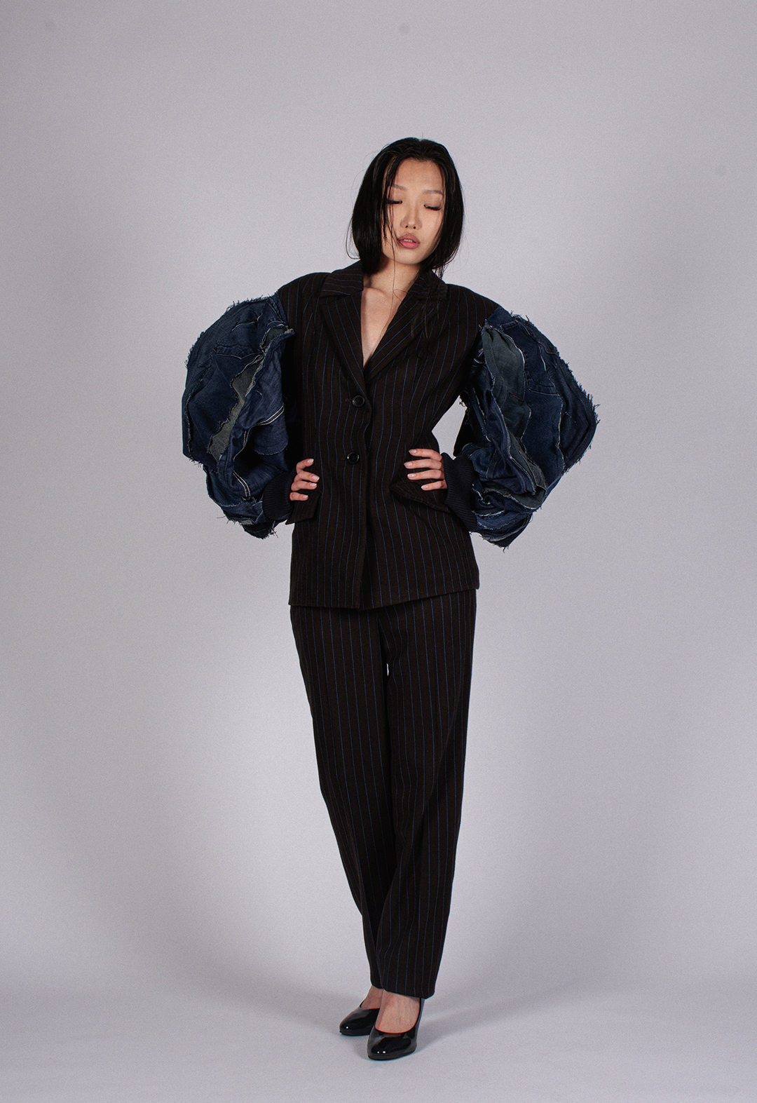 Front view of a model wearing the jacket. The jacket's oversized vintage denim sleeves matched with a pinstripe suit convey the idea of different memories connected together.