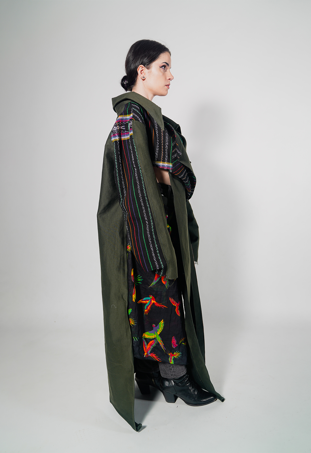 Side view of a colorful artisanal Mayan textile deconstructed trench and matching skirt in army-green silk wool. I draw from the vibrant textiles of Guatemala to create pieces that represent the strength and cultural identity of the Mayan people amid the dissolution of their homelands.