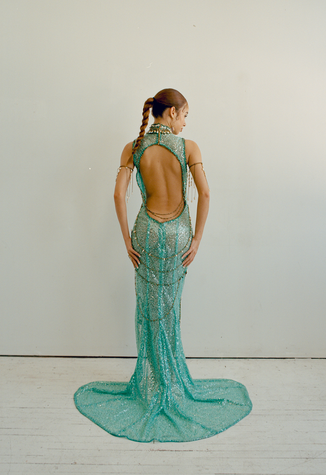 Back view of a model wearing a turquoise beaded dress. There is a big oval cut-out on the back.