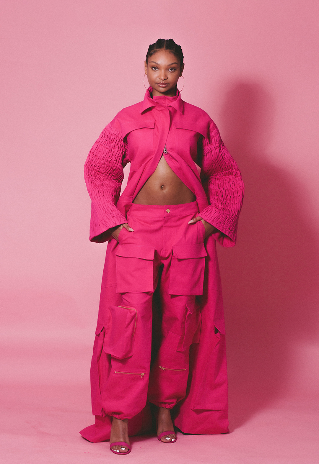 Front view of a model in a hibiscus pink oversized cargo pant and parka, in cotton canvas, with double collar and smocked sleeves.