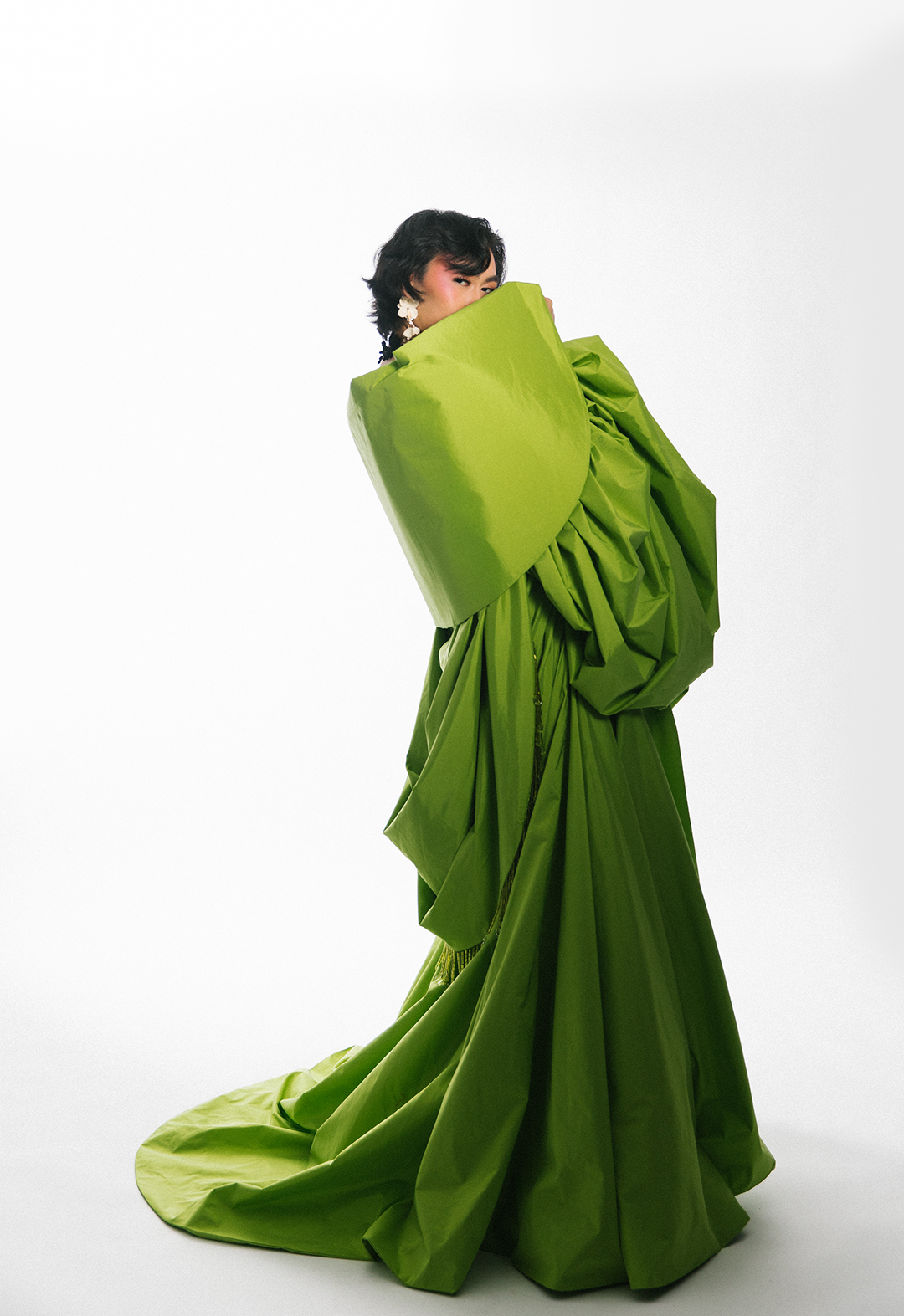 The model is wearing an opera coat that is made of a spring-green taffeta. This photo highlights the back/side view of the coat, showing the collar inspired by the barot saya and a cowl with color-matched, crystal fringe trim.
