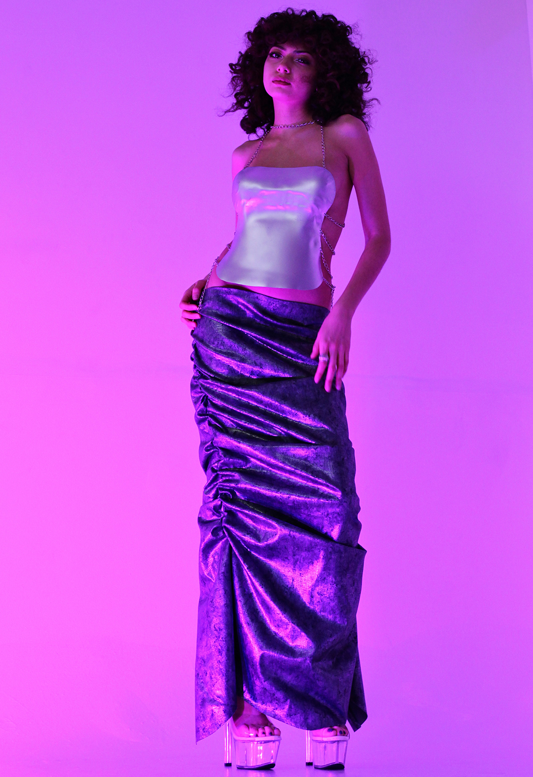 Sofia wears the second look of the Astral collection. As the purple light hits her and the garment, an iridescent shine comes from the handmade Worbla top, casting shine and shadows on the ruched denim floor-length skirt. This look is lengthening and creates a very beautiful silhouette. 