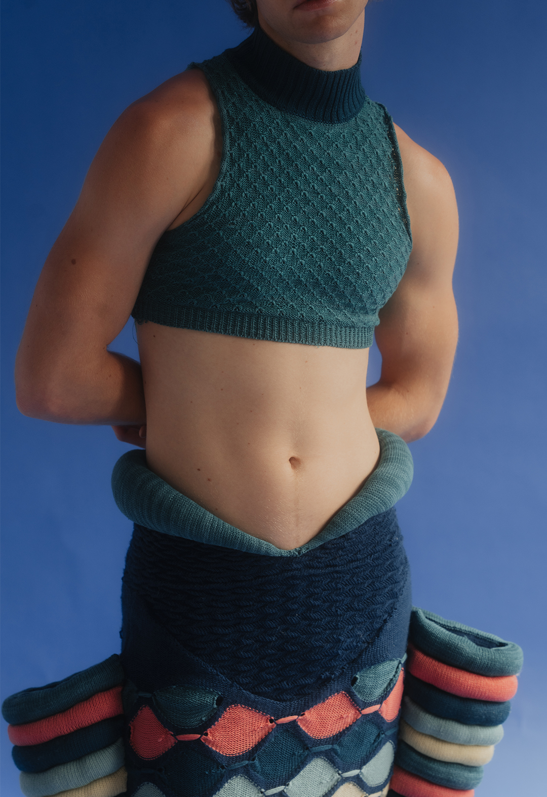 This is a close-up shot of the model wearing a teal knit tank top and a blue, teal, pink, and yellow sculptural skirt.