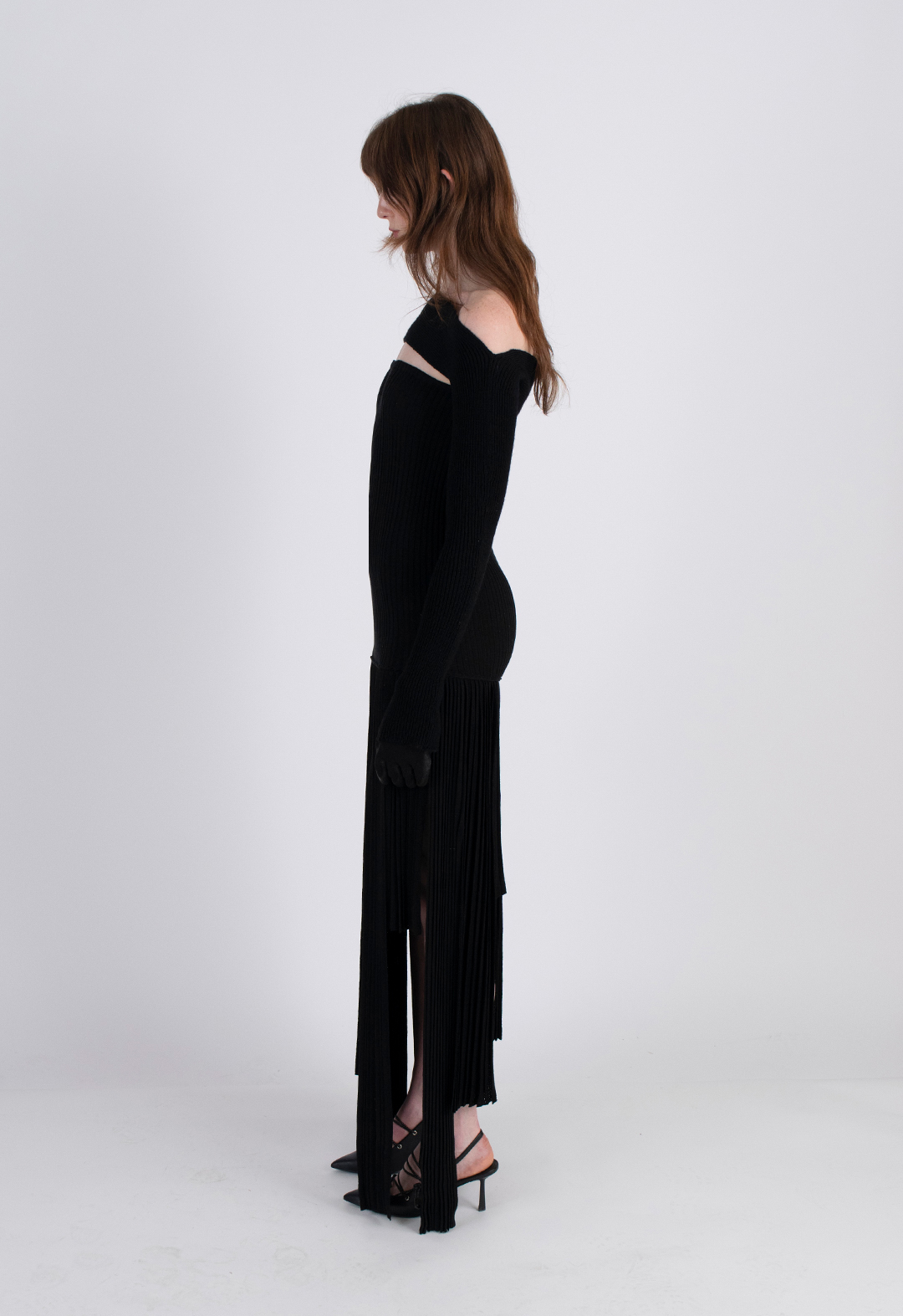 Side view of a model wearing a black knit dress with an asymmetrical hem.