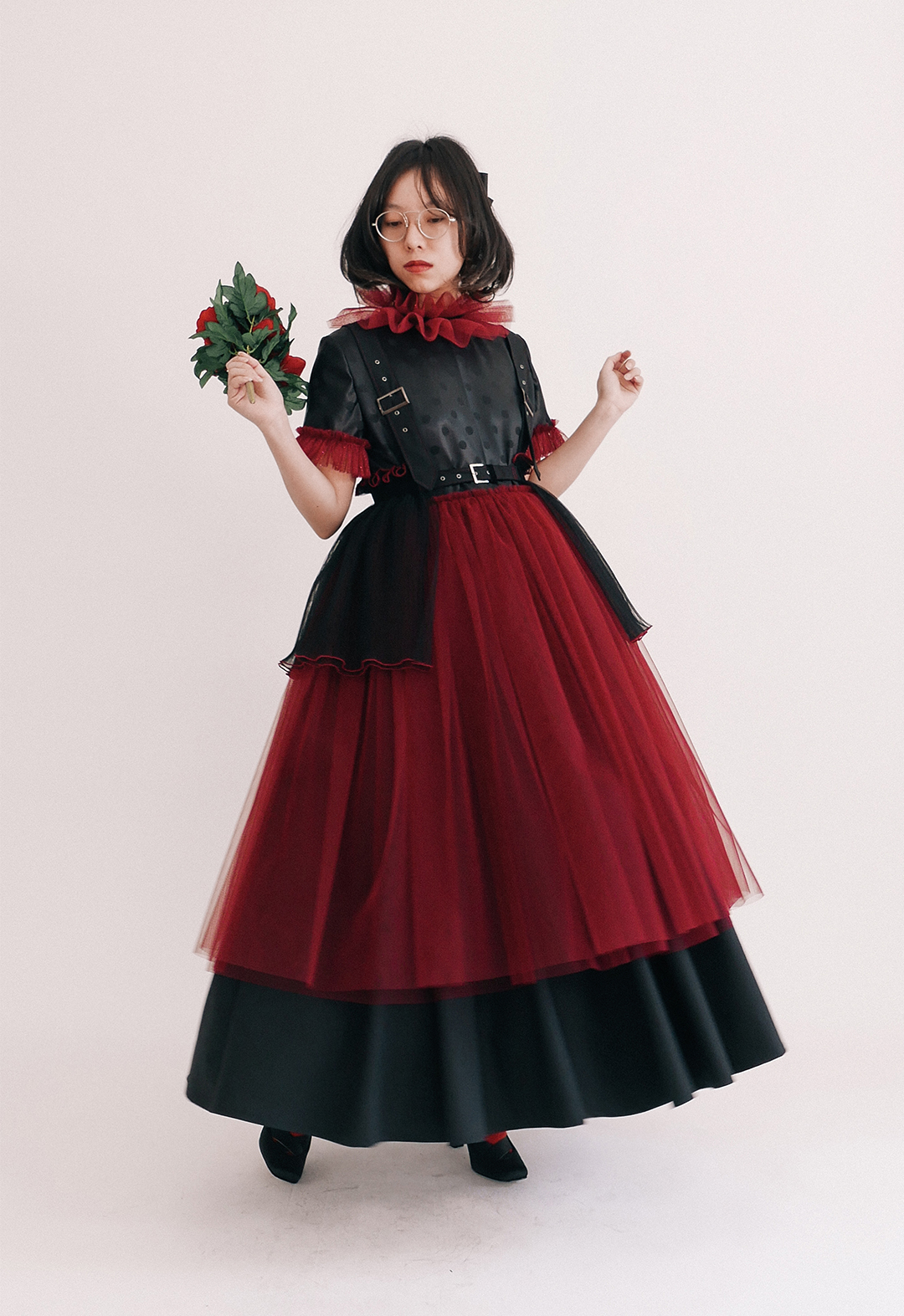 A front view of a model wearing the one-piece dress with suspenders, tulle skirt, and half of the harness. The model is holding a bouquet of roses.