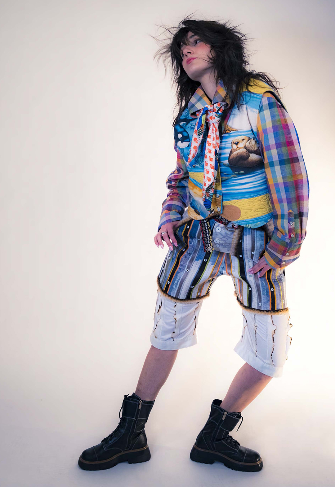 The model wears a waistcoat made from a vintage marine wildlife quilt. It has an adjustable back and a four-button front closure. The multiplaid colored dress shirt was hand weaved and dyed in Cambodia and is 50 percent silk and 50 percent lotus. The bottoms of the look consist of an outer shell short made from seat belt webbing and a printed double-sided bias trim held together with a dense zigzag stitch. Layered under that is a long boxer short made of burnt-edge stripes held together with a dense zigzag stitch, and a three-button cuff on the outside of the leg. The fabric of this garment is made from the eucalyptus plant, sourced from India.  