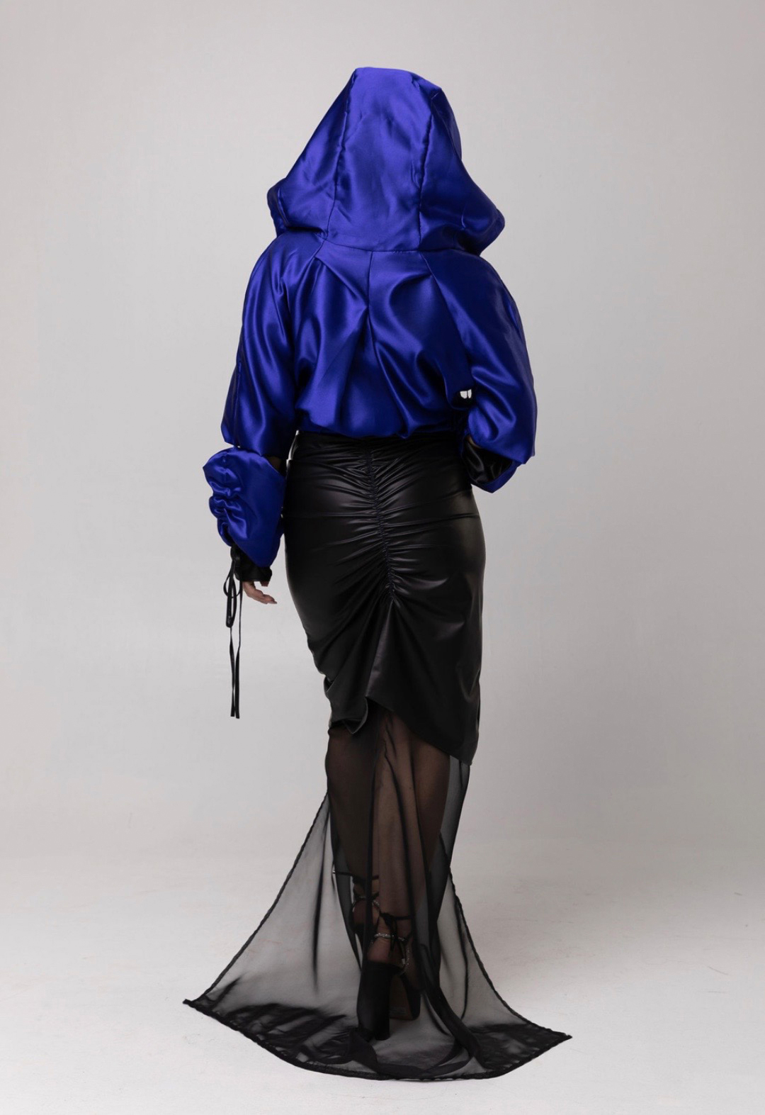 This is a back view of a model wearing a blue jacket and a black skirt, which is the blend of faux leather and chiffon. There is gathers at the center back of the skirt. 