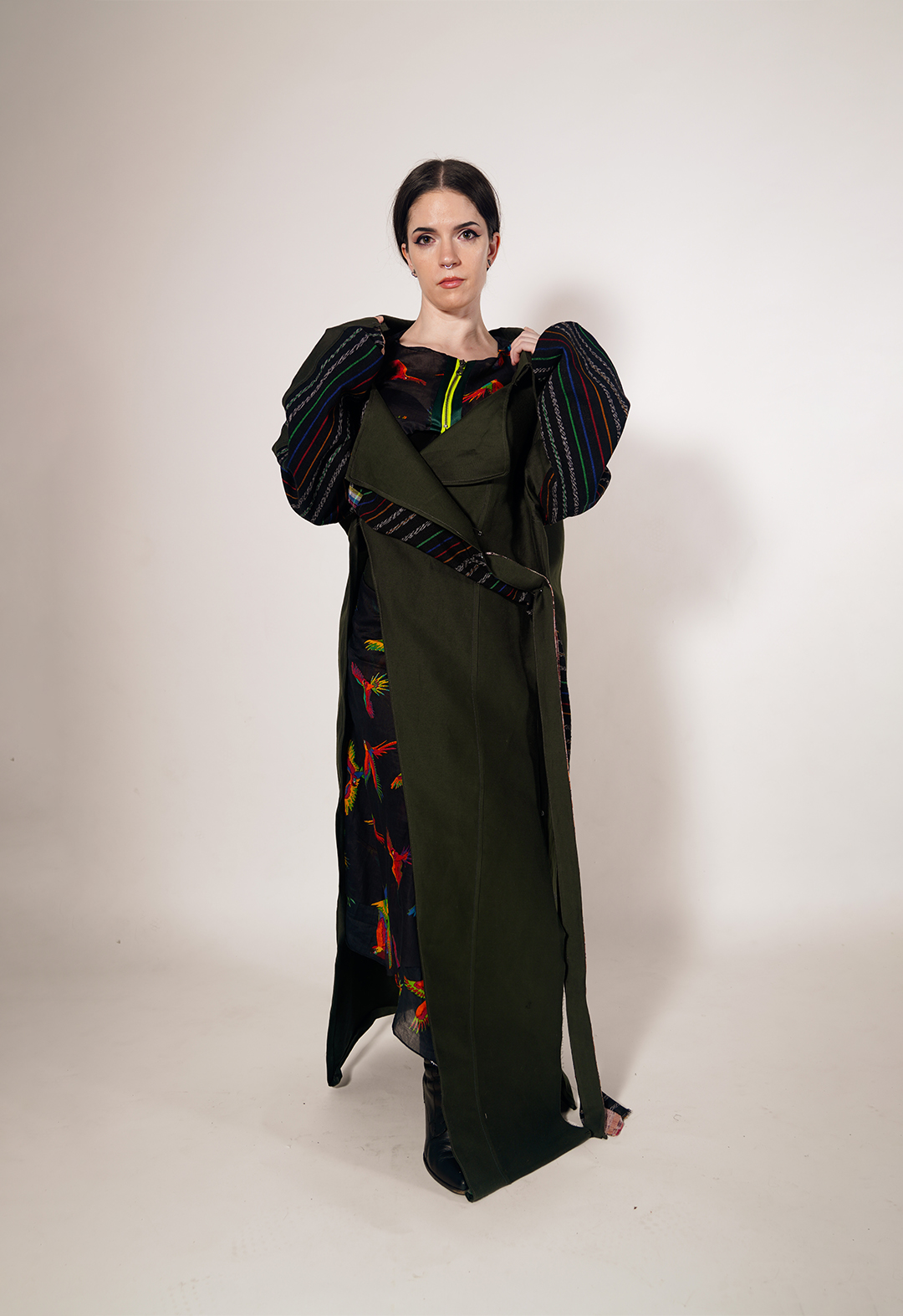 Front view of a colorful artisanal Mayan textile deconstructed trench and matching skirt in army-green silk wool. I draw from the vibrant textiles of Guatemala to create pieces that represent the strength and cultural identity of the Mayan people amid the dissolution of their homelands.