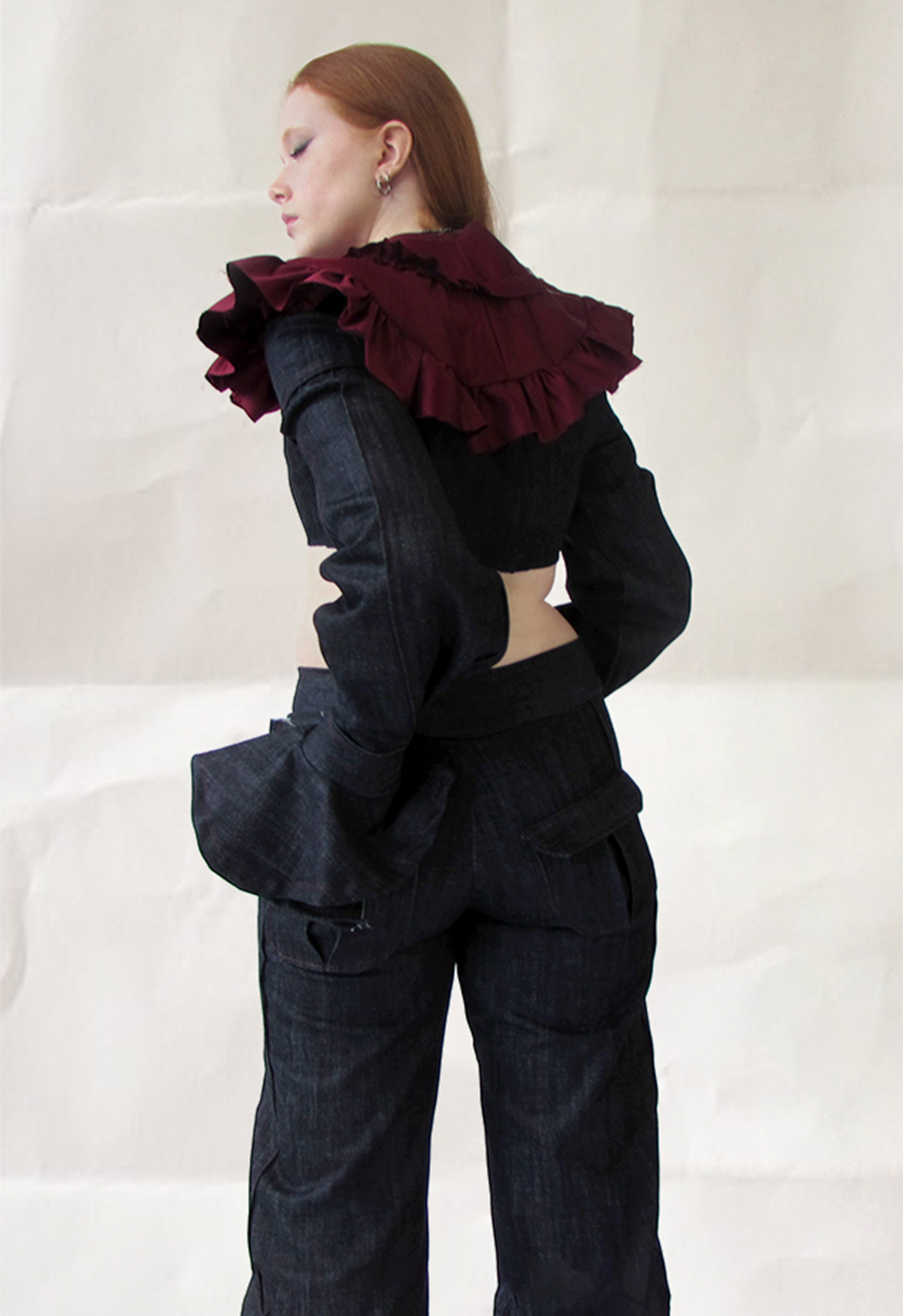 This is a back-view shot of a model in denim trousers with back-pocket detail, paired with a denim top with flare sleeve and a removable blood ruffle collar. 