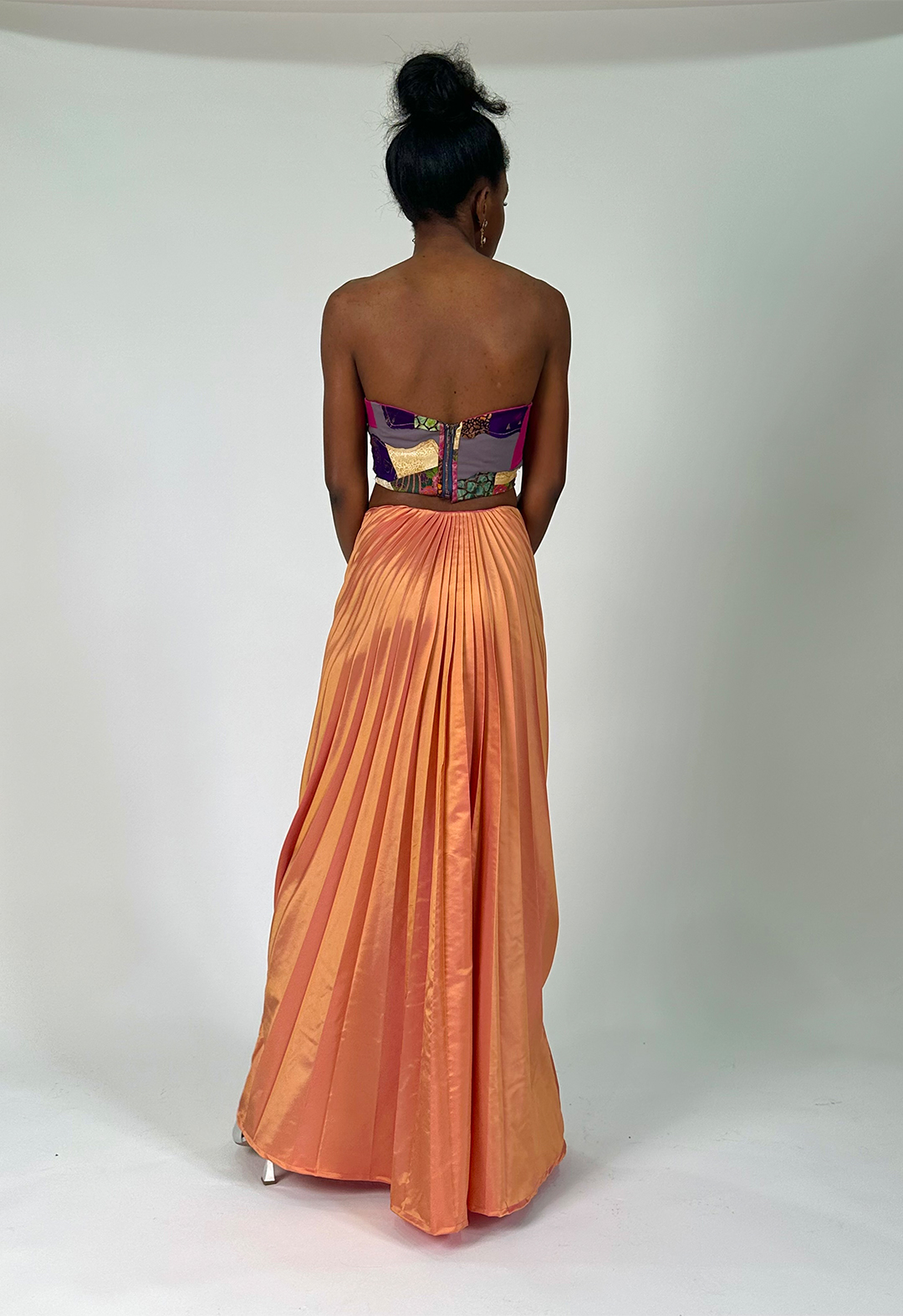 Model’s back is facing the camera, showcasing the concentration of pleats in the back of skirt and the lower back's slight V-closure of the bodice.
