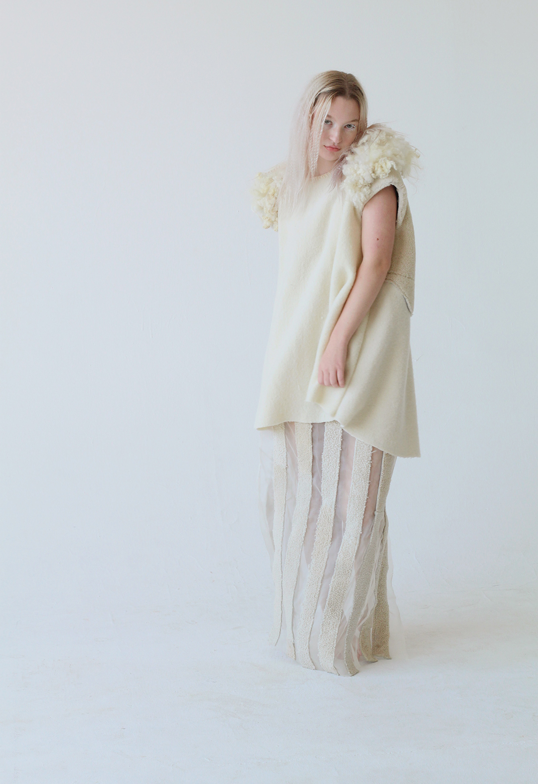 The photo shows the model standing in a sheer skirt made of silk organza, topped with lambskin shearling leather strips in a vertical stripe orientation.