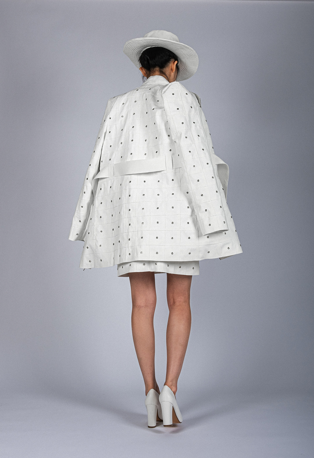 A model is wearing a white ultrasuede coat, a double-layered jacket, an A-line mini skirt, and a hat. 