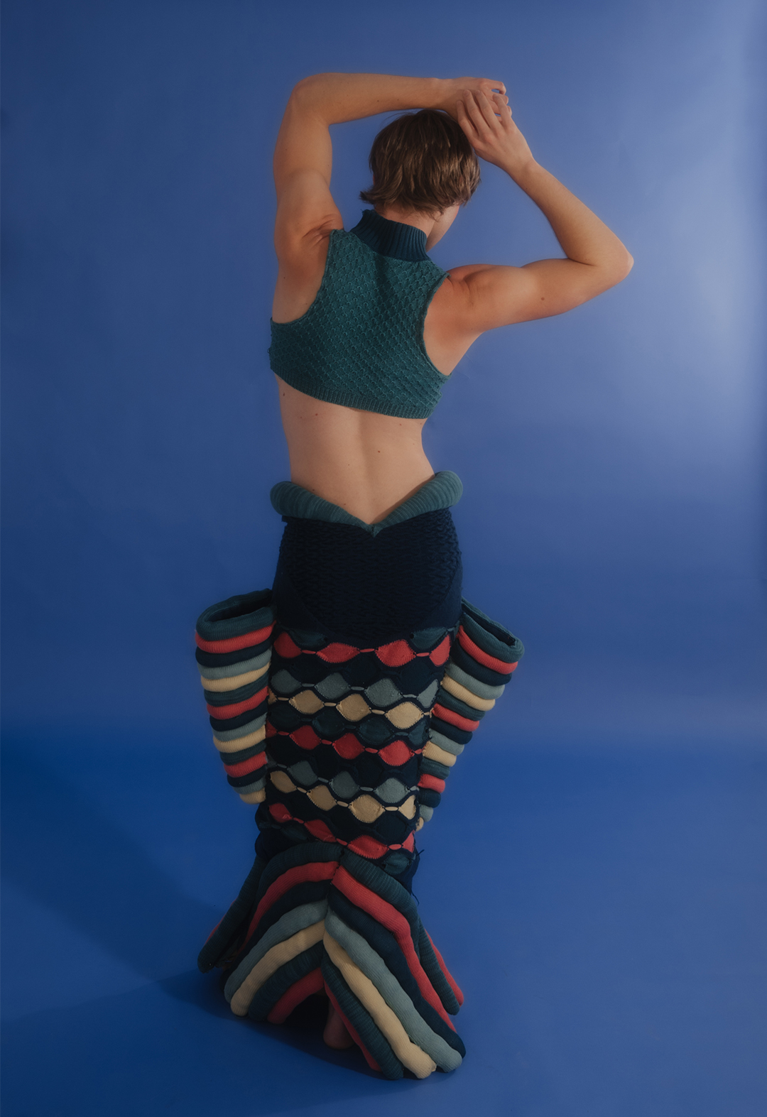 The photo shows a back view of the model wearing sculptural skirt and tank top.