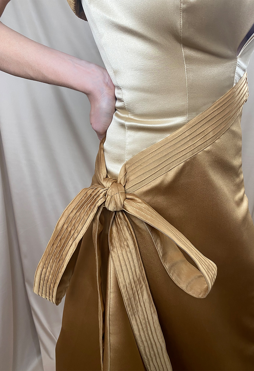Close-up image of a pin-tucked belt tied into a bow on a two-toned garment with an asymetrical skirt.