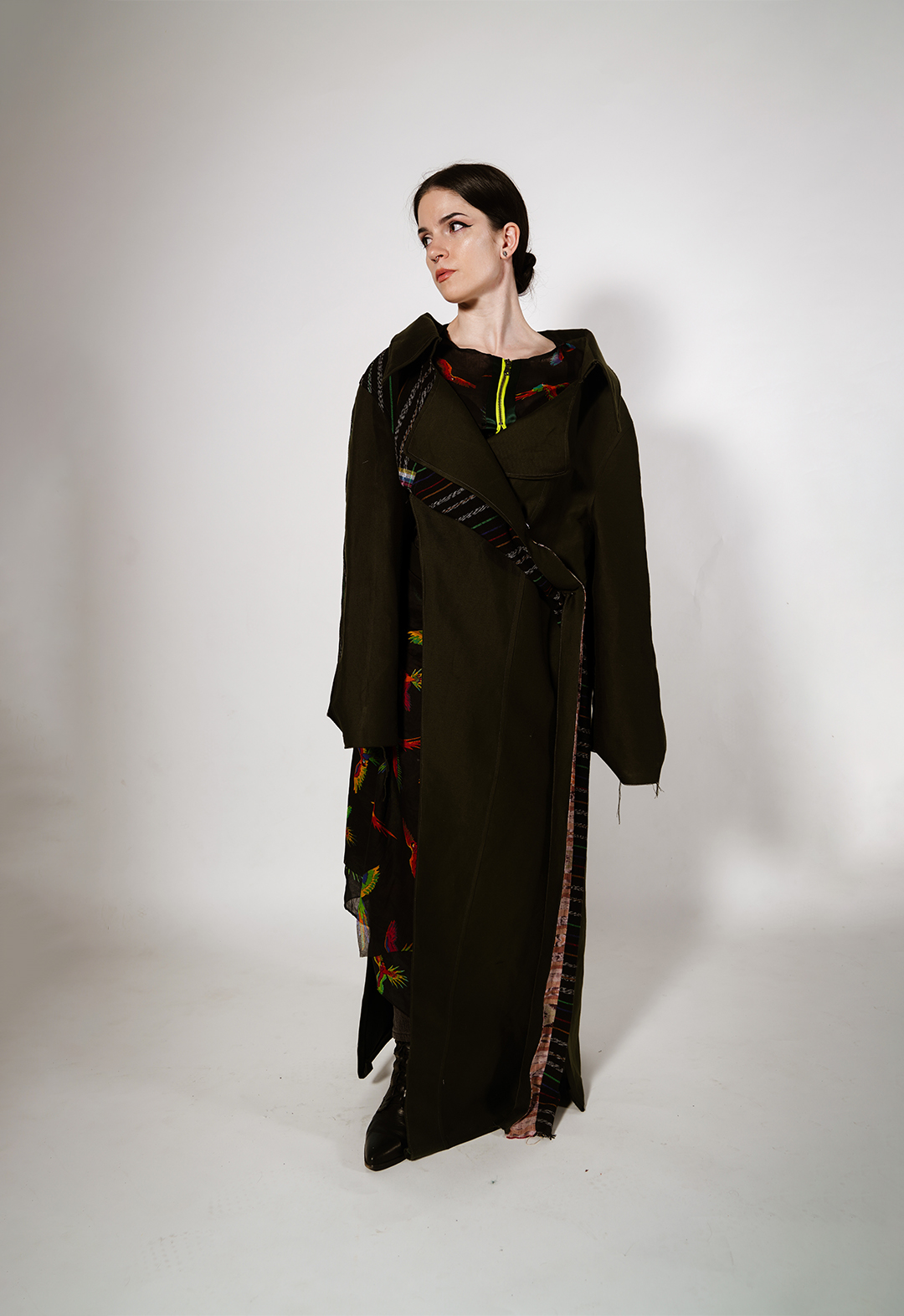 Front view of a colorful artisanal Mayan textile deconstructed trench and matching skirt in army-green silk wool. I draw from the vibrant textiles of Guatemala to create pieces that represent the strength and cultural identity of the Mayan people amid the dissolution of their homelands. 
