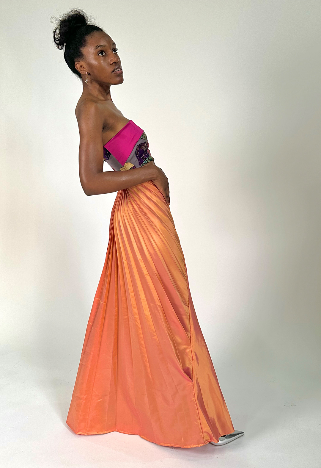 Model leans back while taking a step, showing the flow of the draping of the pleating, while hands are placed at the front.