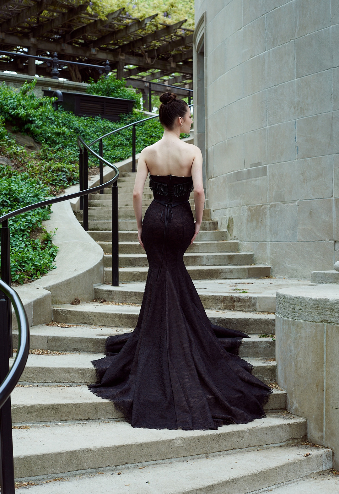 Back view of model standing with hands resting on low hips. Full body shot with neutral stone background staircase.