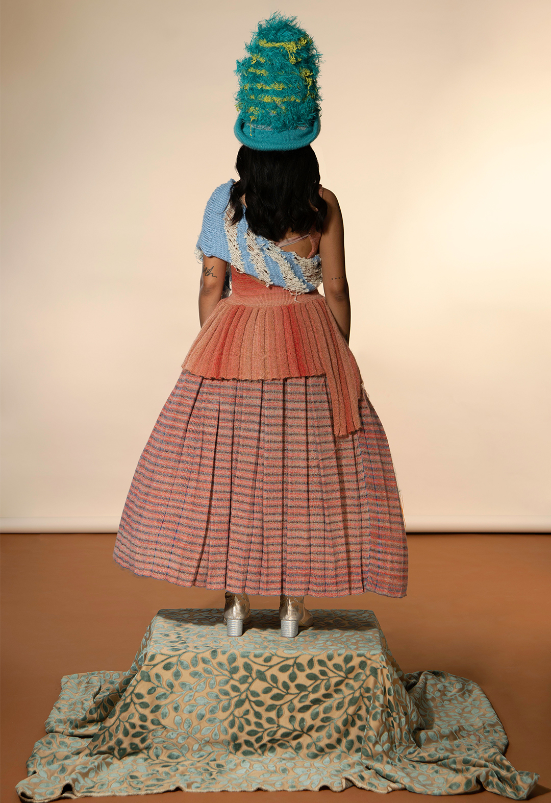 Back view of striped mixed mélange pleated full skirt and pleated hem top with cut-outs and a textured hat.