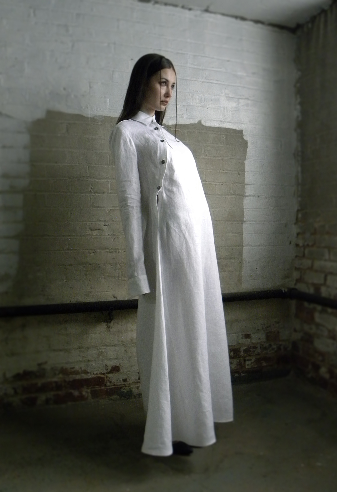 3/4 view of a model leaning back. She is wearing a screen-printed meandering placket shirt dress with white linen and runic buttons.