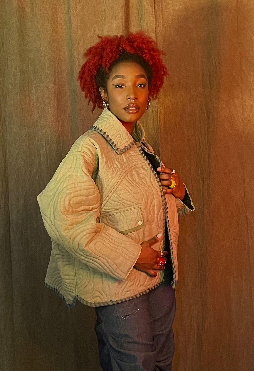 A model is standing with one hand on the jacket, which has a quilted pattern that depicts different imagery.