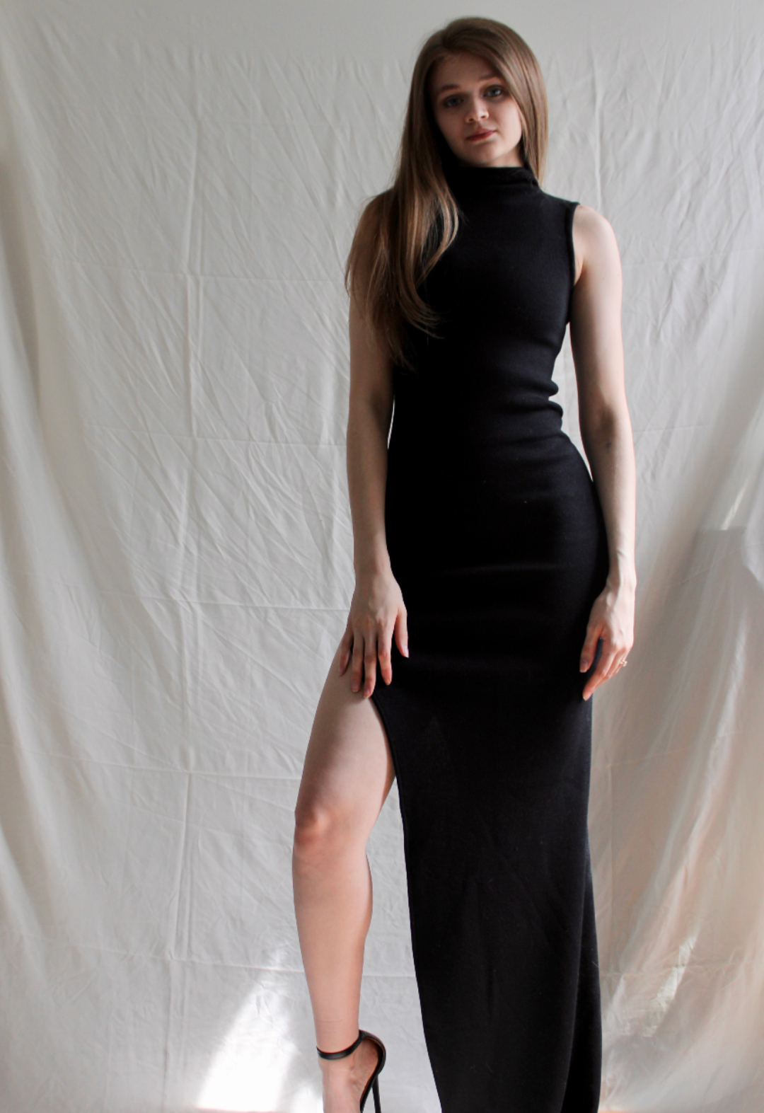 Front view of a model wearing a black knit dress with high leg slit. The background is white.