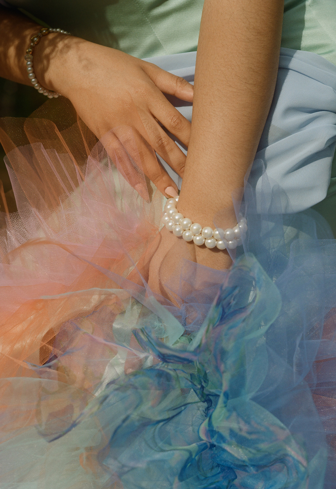 Close-up view of where the ruffles start on the bottom of the gown. The model's hands are on her thighs. She is wearing two pearl bracelets on one wrist. 
