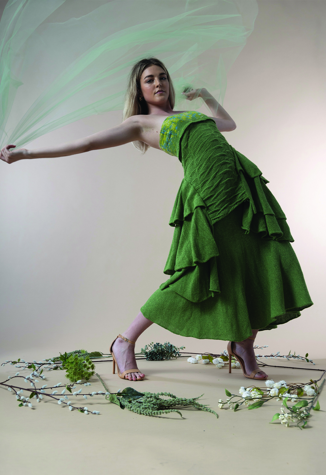 A female model holding a green net veil stretches backward, creating a dramatic movement. 