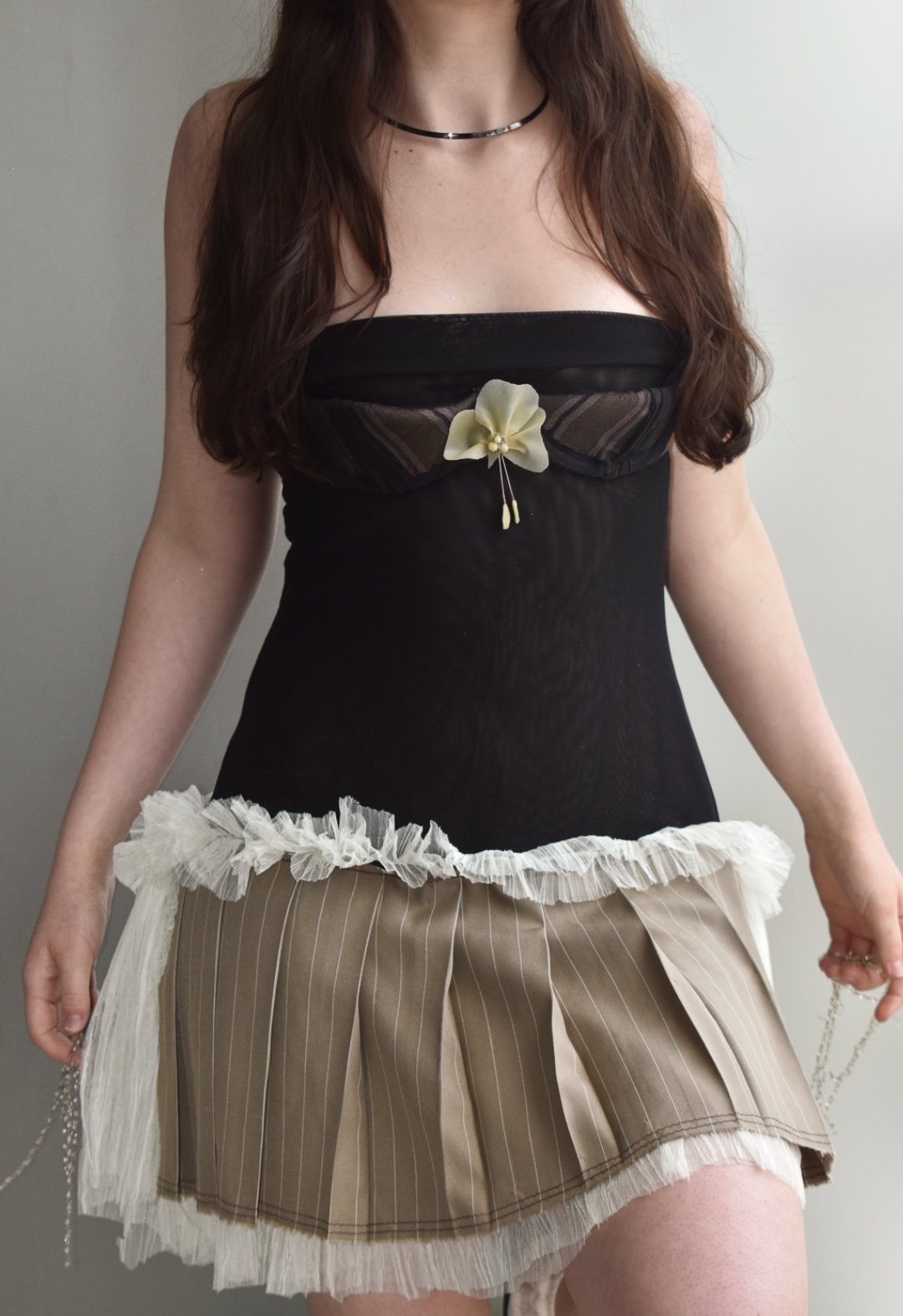 A detail image of the dress, featuring a muted striped bustier, latex flower, and pinstriped pleats.