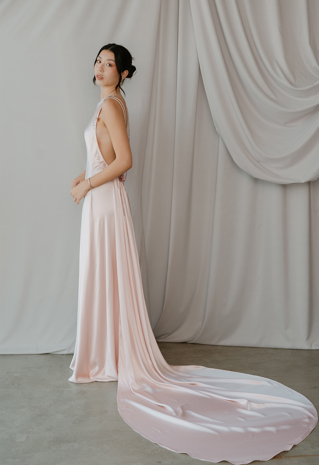 Side view of blush silk crepe back satin bias dress. Low back with loose drape, Swarovski crystals, and lace appliqué. 