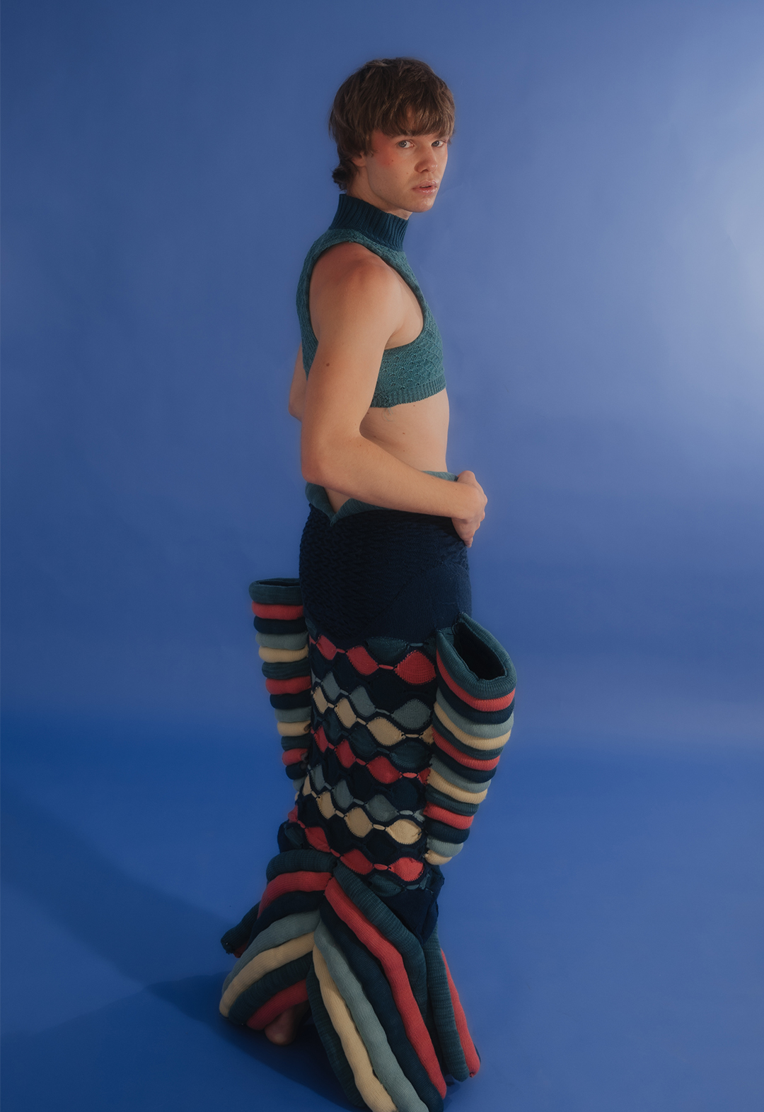 The photo shows a three-quarter back view of model wearing a multicolored sculptural fish skirt and tank top.