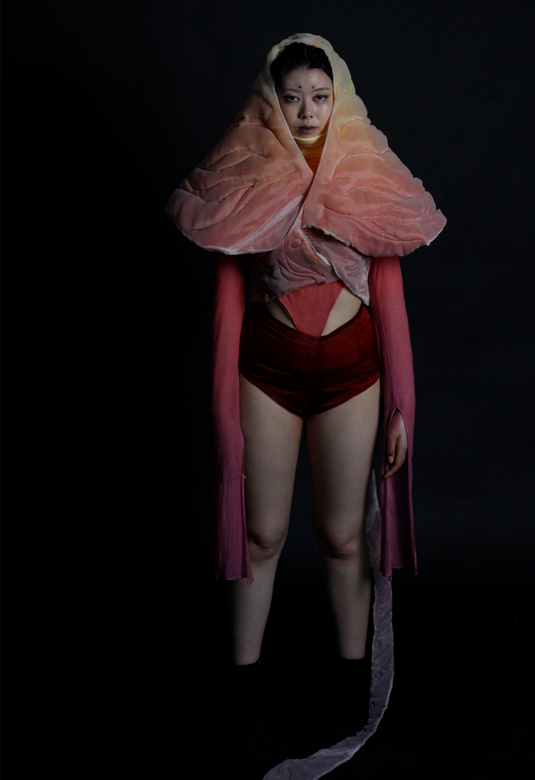 The photo shows a front view of the model in an ombre-colored cape and knit top, matched with silk mini shorts. The cape is made with a zero-waste pattern.