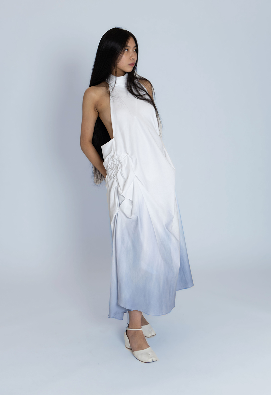 A model presents the front view of a white cotton dress dyed blue at the bottom.