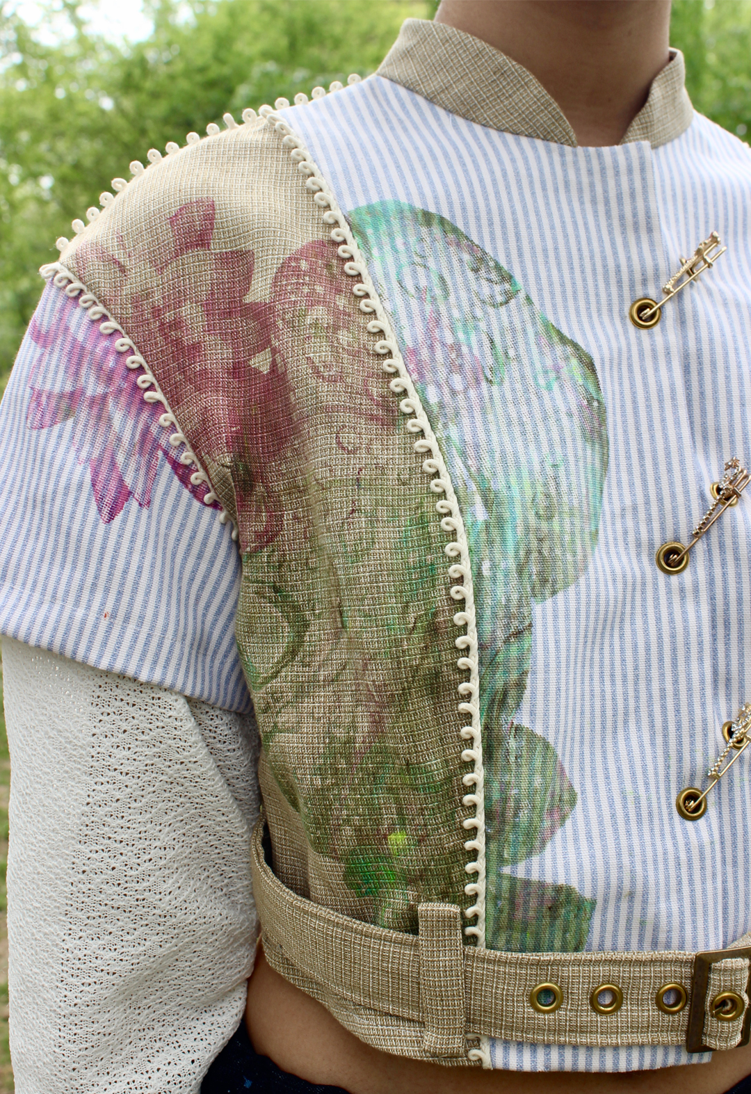 Close-up front view of button-up top, featuring lotus flower screen print, piping with loop shapes, and three gem-detailed safety pins across the front.