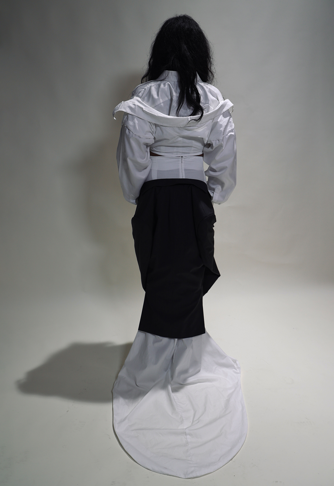 Back view of layered white shirts hanging from the shoulders. Skirt train with deconstructed jacket.