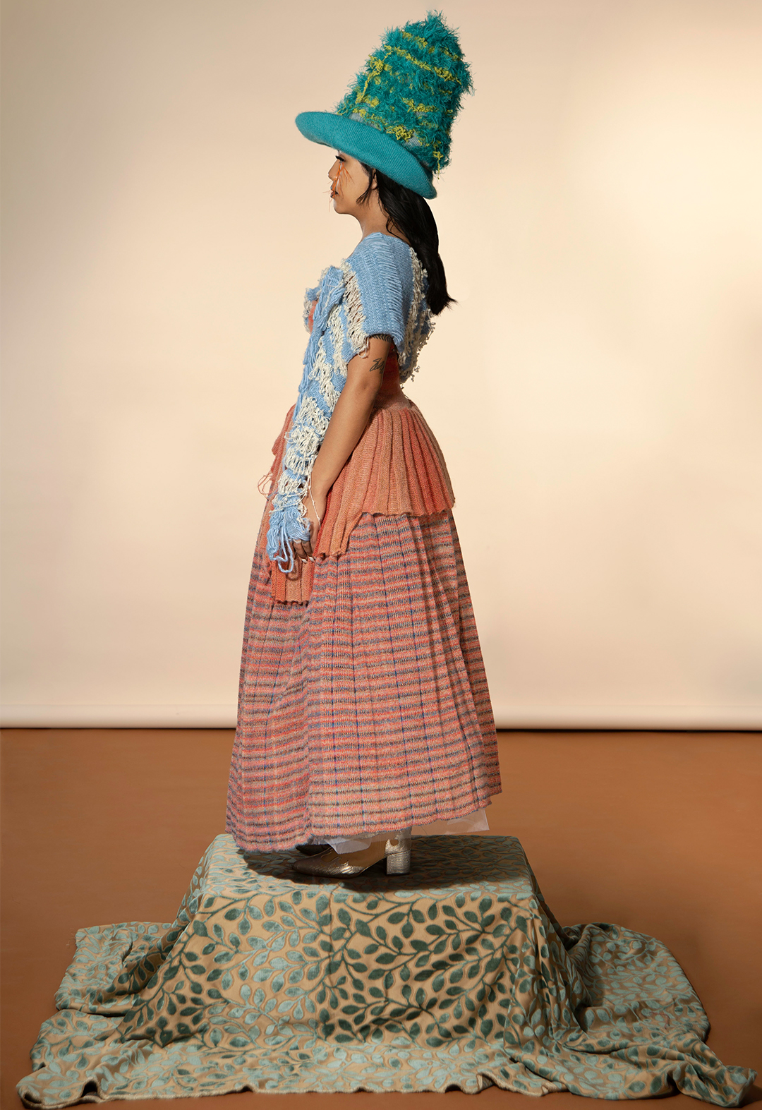 Side view of striped mixed mélange pleated full skirt, a pleated hem top with cut-outs, and atextured hat.