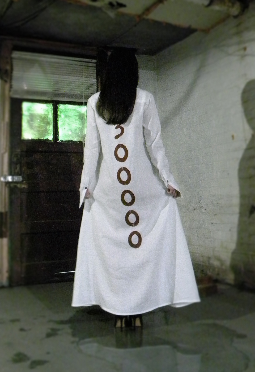 Back view of a model wearing a screen-printed meandering placket shirt dress made of white linen with runic buttons.