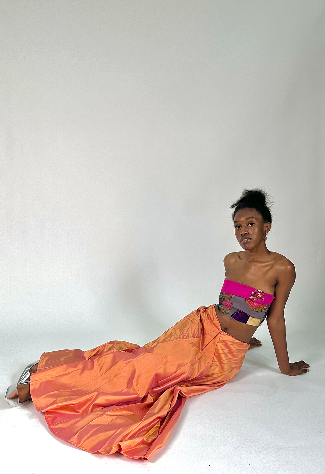 Model lays on side with hands propping them up on the floor, while the skirt is placed around, showcasing the flow of the pleats and the two-toned nature of the taffeta fabric.