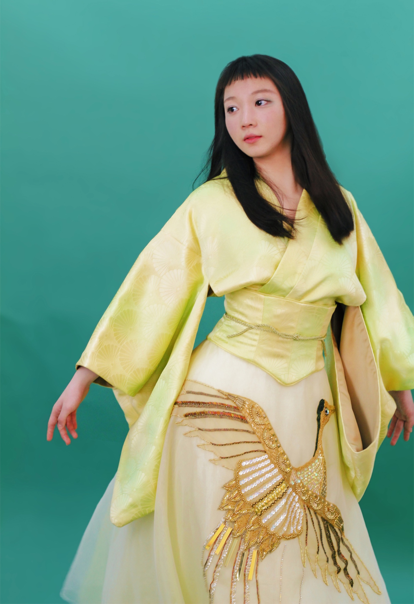 A ballerina in a yellow silk kimono-inspired dress looking off to the side in front of a green background. 