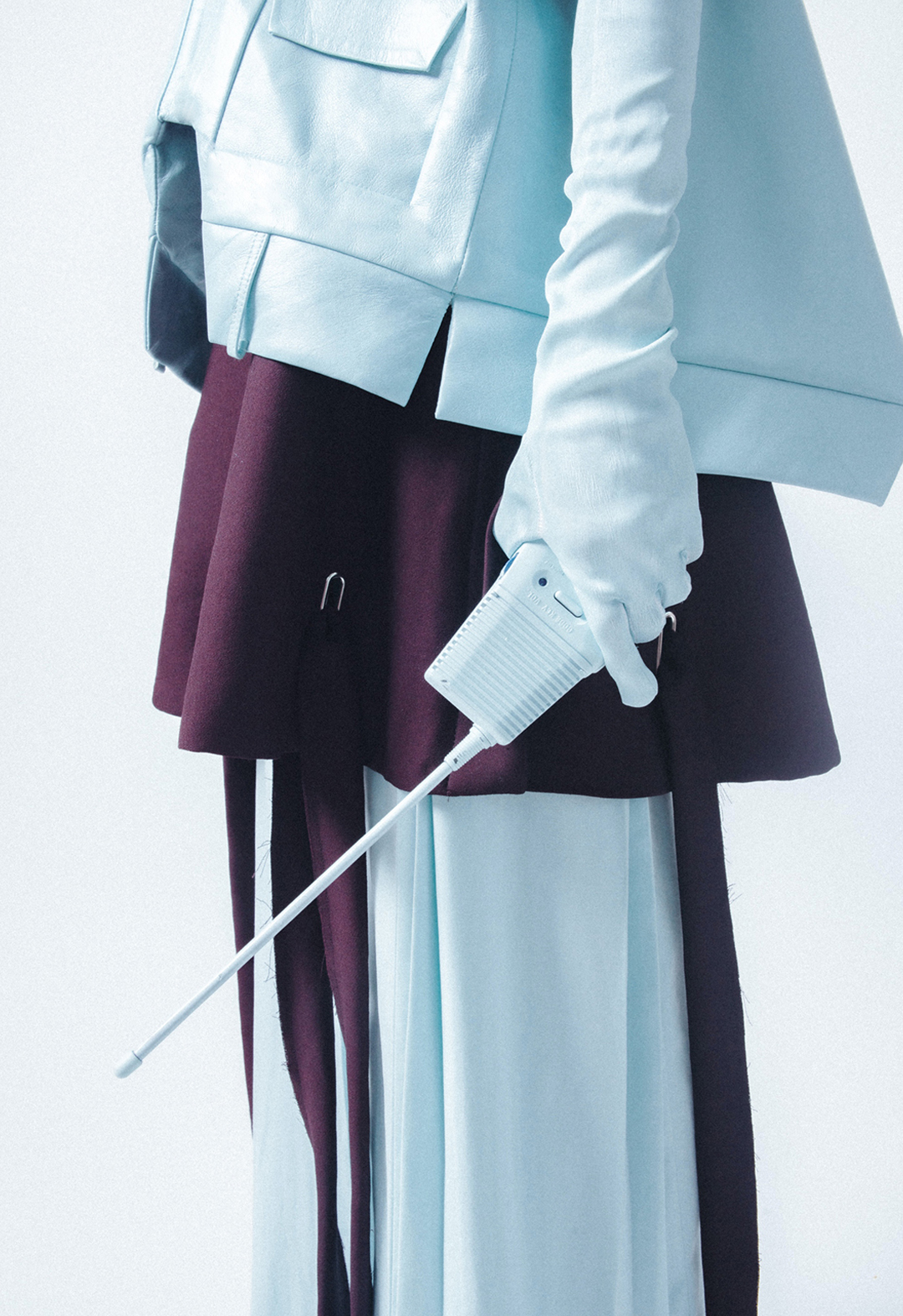 Detail view of look 2, showing a baby-blue, double-collar leather shirt jacket with trapunto details and a back opening, a baby-blue double-pleated skirt, and a dark-purple grommet apron skirt.