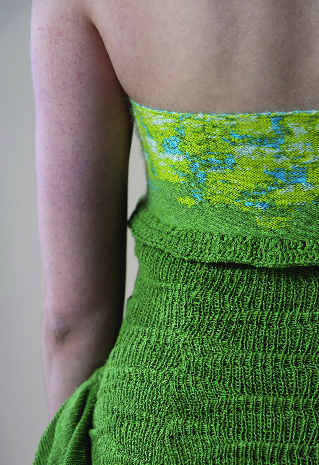 Close-up view of the left side of the model's back, showing the detail of the tube top, consisting of a green, yellow, sky-blue, and white abstract pattern; part of the bumpy bodice; and the side flare trim.