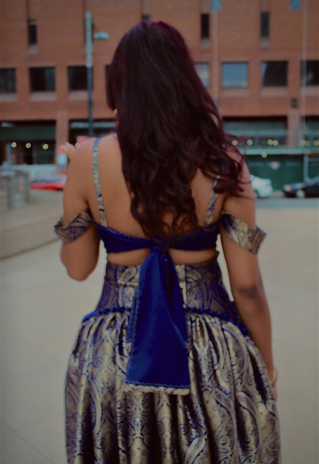 Back view of a model wearing a top that can be tied the back. The ties have the brocade as details in the ends as well as the same gold top stitching detail as the rest of the top. 