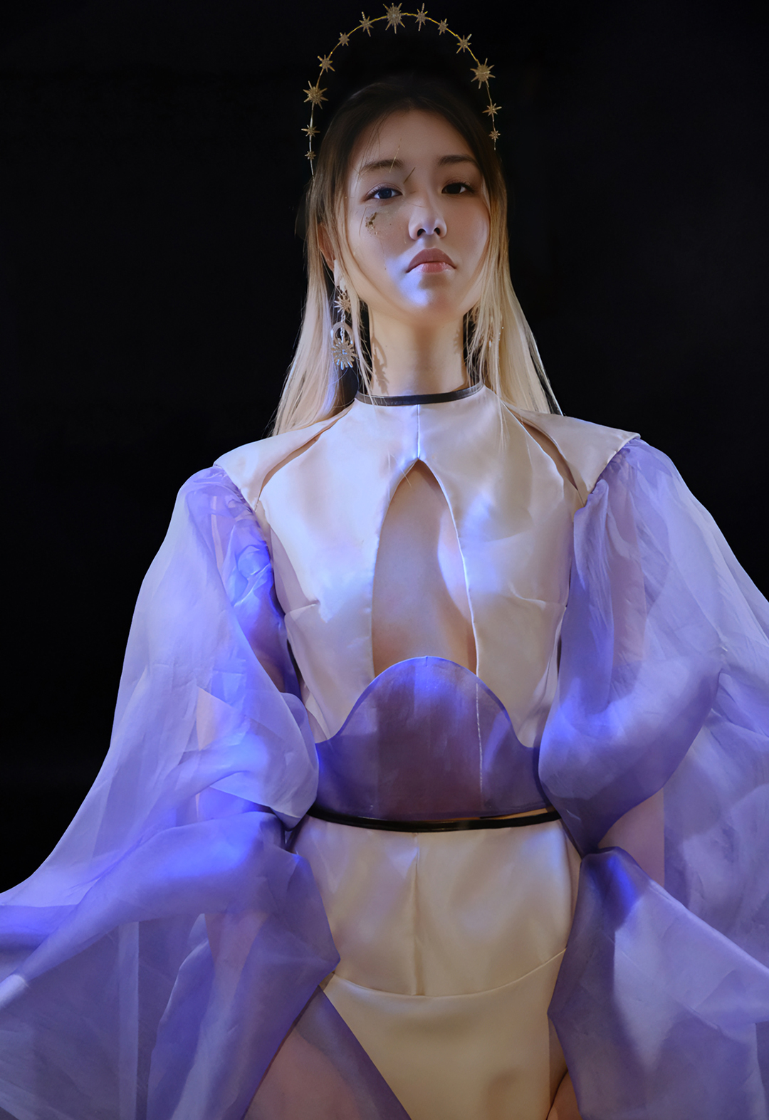 front view of a model wearing a white top with purple sleeves. There is a center front cut out and two small cut-outs at the collar bone. The background is black.