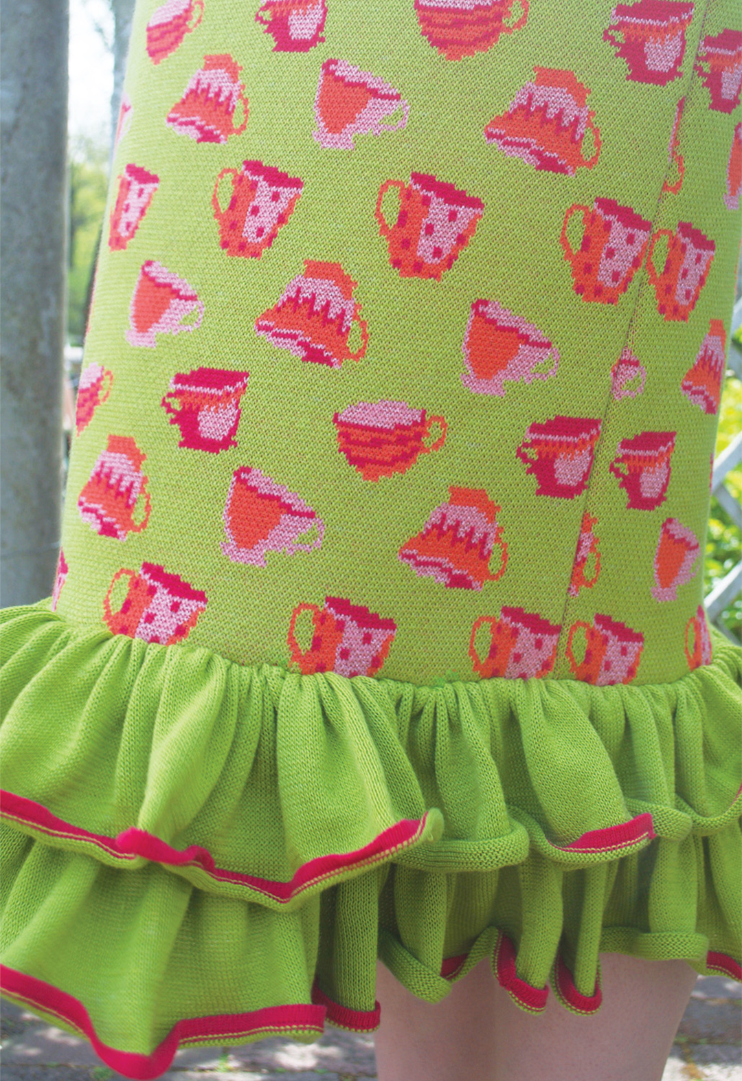 Zoomed-in photo of the multicolor teacup print and ruffle hem on a green jacquard knit dress. 